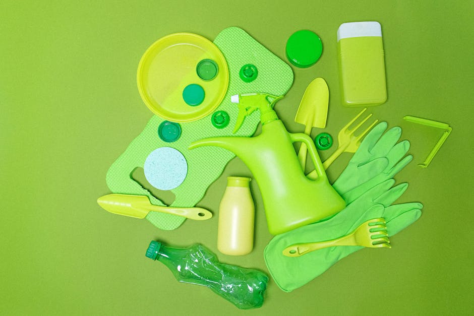 A collection of green cleaning and gardening tools and accessories arranged on a bright green background. Visible items include a plastic watering can with a long spout, a small spray bottle, a pair of rubber gloves, a dustpan with a handle, a small hand rake, a plastic bottle, and several circular lids or covers. There is also a rectangular sponge with rounded edges, a small trowel, and a few small containers or pots, all predominantly in shades of green and yellow. The items are laid out in a somewhat scattered manner, with some objects overlapping or placed at slight angles, creating a visually organized scene related to outdoor or home cleaning and maintenance tasks. The bright, uniform background enhances the vivid color of the tools, typically associated with waste or rubbish management in domestic or outdoor settings, reflecting a focus on outdoor or on-site disposal and collection activities associated with private waste handling services.